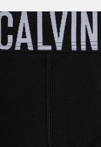 Zwarte katoenen boxershorts met een grijze elastische band waarop "CALVIN" staat. De stof is glad met een lichte glans en heeft geen zichtbare patronen.