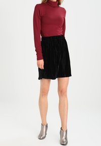 Burgundin turtleneck-top, joka on yhdistetty mustaan, laskostettuun samettihameeseen ja hopeisiin nilkkasaappaisiin. Asusteessa on tiukka siluetti ja sileät tekstuurit.