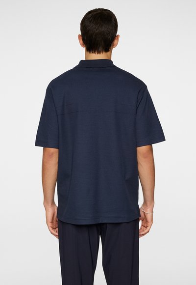 Marineblå kortærmet polo shirt, bomuldsblanding, lige snit, med rygpanel og syningdetaljer. Ideel til afslappet brug.
