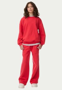 Sudadera roja de corte oversize, con puños acanalados, combinada con pantalones de chándal rojos a juego, llevada con zapatillas blancas. Textura suave, estilo casual.