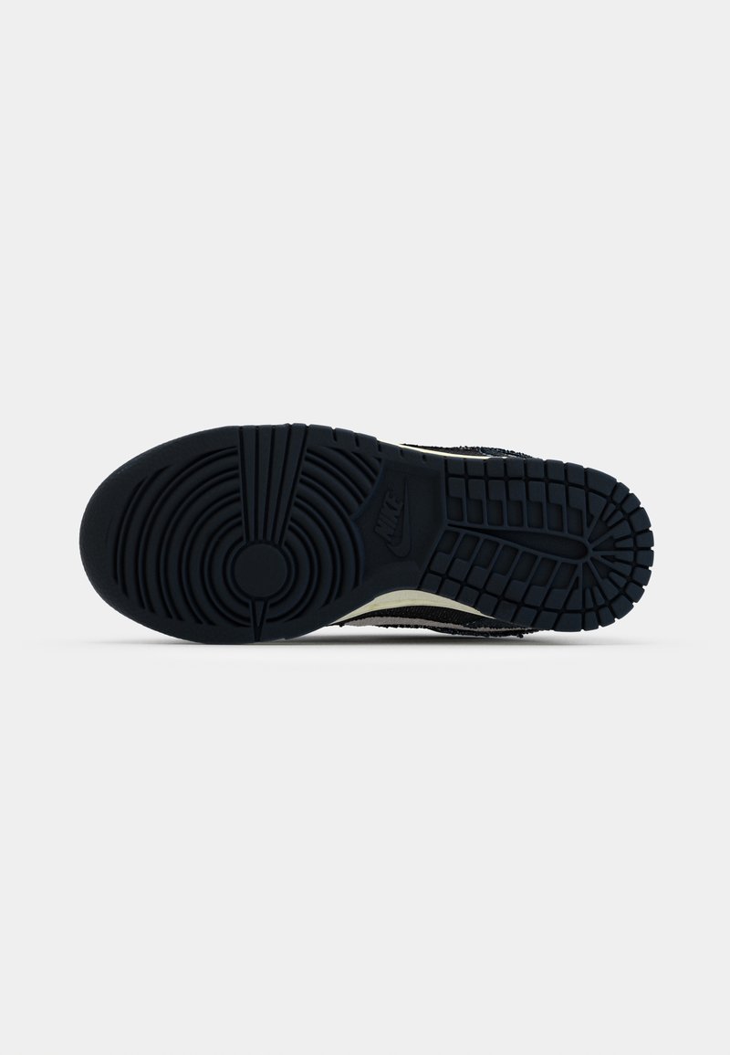 Semelle de chaussure en caoutchouc noir avec des motifs texturés, présentant un logo circulaire et des accents striés. Dessous lisse, conçu pour une bonne adhérence.