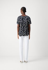 Top corto a maniche corte nero con stampa di margherite bianche, con dettaglio plissettato sulla schiena, abbinato a pantaloni bianchi a gamba dritta e scarpe con tacco blocco beige.