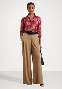 Floral-patterned, pink long-sleeve button-up shirt, paired with beige wide-leg trousers, cinched with a black belt, and black heeled sandals.