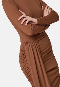 Langärmliges braunes Kleid mit gerafften Seitendetails und einer glatten Textur, das eine taillierte Silhouette und einen weichen Stoff aufweist.