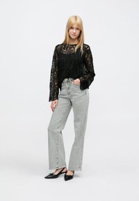 Juodo nėriniuoto audinio ilgomis rankovėmis palaidinė laisvo silueto, derinama su šviesiai pilkomis, aukštu liemeniu ir plačiomis kojomis džinsais. Rinktinė aprangą užbaigia juodi bateliai be kulno.