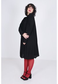 Zwarte jurk met een gesmokt bovenlichaam en lange geplooide mouwen. Draagt het met rode tights en zwarte blokhakken. Gladde textuur.