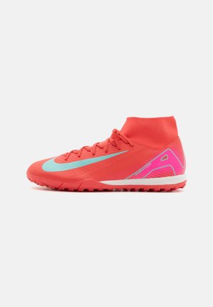 Leuchtend orangefarbener Fußballrasenschuh mit hohem Knöchelkragen, blauem Nike-Swoosh, pinken Fersendetails und strukturierter Sohle für das Spielen im Freien.