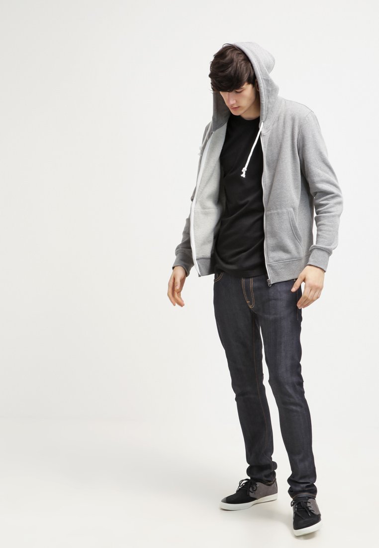 Grå zip-up hættetrøje med snørebånd, båret over en sort skjorte, parret med mørke denimjeans og sorte sneakers. Afslappet pasform og stil.