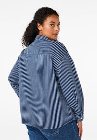 Maglietta a maniche lunghe a righe blu marine e bianche, realizzata in tessuto leggero, con colletto a bottone e vestibilità comoda con orlo arrotondato.