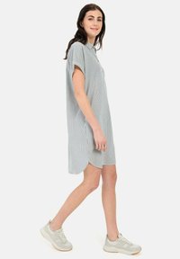 Gestreiftes Hemdkleid in Hellblau und Weiß mit kurzen Ärmeln, abgerundetem Saum und strukturiertem Stoff; kombiniert mit hellgrauen Turnschuhen.