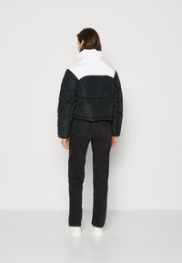 Giacca a vento nera con pannello superiore bianco, design corto, texture lucida e colletto alto. Abbinata a jeans scuri e sneakers bianche.
