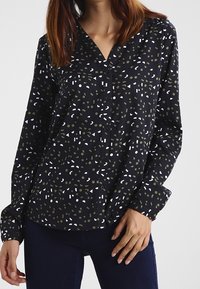 Maglietta nera a maniche lunghe con scollatura a V, caratterizzata da un motivo misto di verde, bianco e forme geometriche; tessuto leggero e apertura con bottoni.