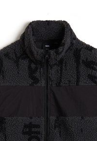 Schwarze Fleecejacke mit Reißverschluss und hohem Kragen. Sie hat ein kontrastierendes matt-schwarzes Panel über der Brust und eine strukturierte Oberfläche.