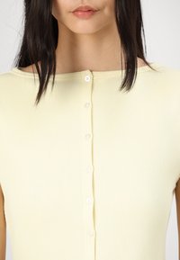 Yellow ribbed tank top with a boat neckline, featuring a central row of white buttons and a fitted design. Smooth texture and short sleeves.