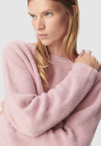 Jasnoróżowy sweter wykonany z miękkiego, puszystego materiału, charakteryzujący się luźnym krojem, szerokim dekoltem i długimi rękawami. Prosty, jednolity design.