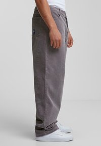 Grijze corduroy broek met een losse pasvorm, voorzien van verticale ribbels, zijzakken en een logolabel op de achterzak. In combinatie met witte sneakers.