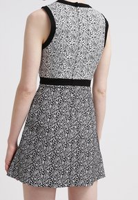 Svart och vit mönstrad klänning med en åtsittande bodice, utställd kjol och kontrasterande svart kant. Slät tyg med blommönster.