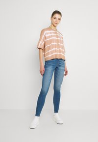 Braunes Batik-T-Shirt in Übergröße mit weißen Streifen, kombiniert mit blauen Skinny Jeans und weißen Plateausneakern. Einfaches und lässiges Design.