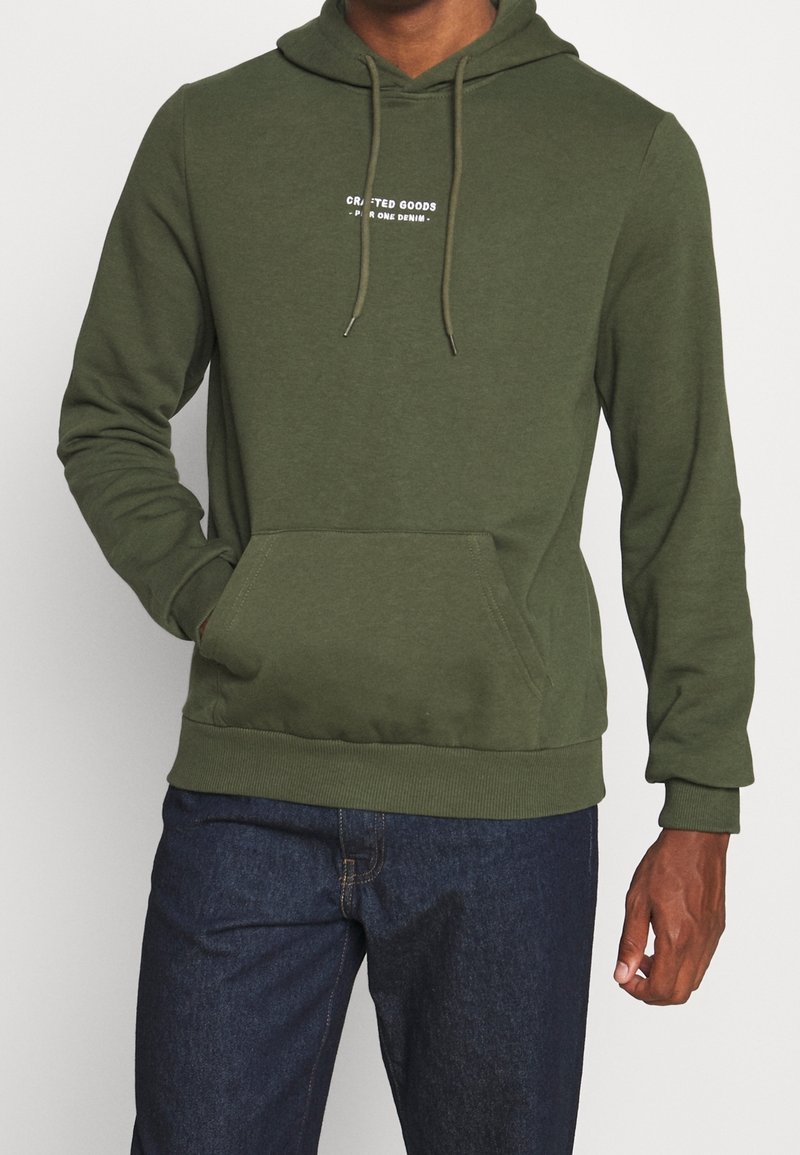 Sudadera verde hecha de una mezcla de algodón. Presenta un bolsillo frontal, cordones en la capucha y texto impreso en el pecho. Textura suave.