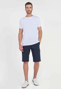 Witte t-shirt met ronde hals, marineblauwe cargoshorts met zijzakken, gedragen met witte sneakers, met een eenvoudig en casual ontwerp.