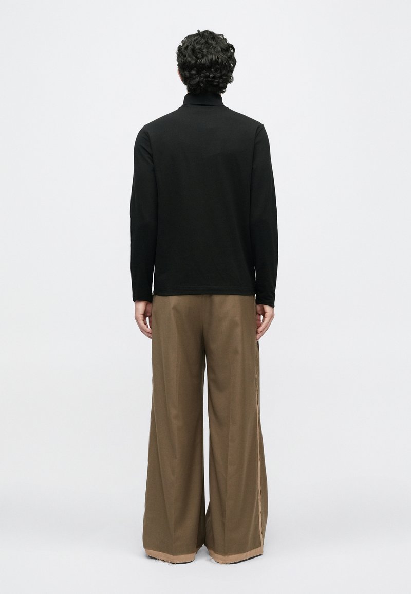 Sort langærmet top med høj krave, parret med brede brune bukser med en kontraststribe langs siden.