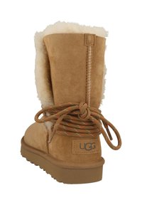 Tan suede boot with a fluffy shearling cuff. Features a decorative lace at the back and a rubber sole. UGG logo on the heel.