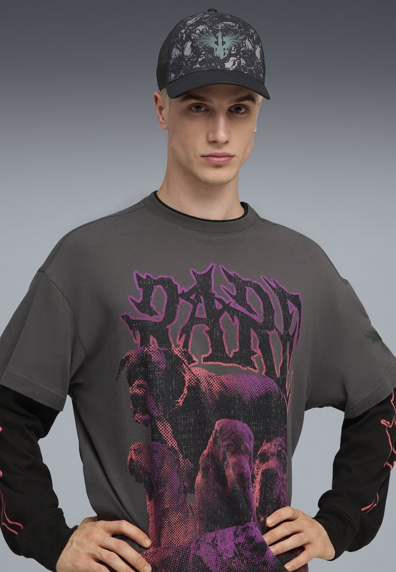 Czarna czapka z wzorzystym szarym wzorem i turkusowym logo, w połączeniu z ciemnoszarym t-shirtem z różowym nadrukiem psów.