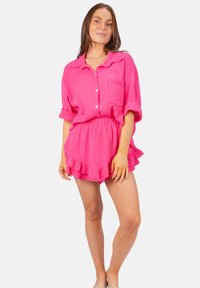 Ensemble en coton texturé rose, comprenant un haut à bouton avec une poche et un bas de short à volants. Manches courtes et coupe décontractée.