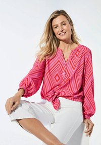 Roze blouse met knopen en een geometrisch patroon, met lange mouwen en een geknoopt zoom. Gemaakt met witte cropped broek.
