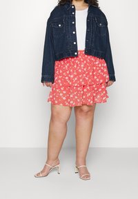 Denim jacket with cropped design, button closure, and two front pockets; layered coral dress with white floral pattern; nude strappy heels.