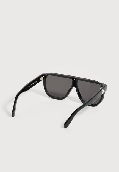 Lunettes de soleil noires surdimensionnées avec des verres rectangulaires foncés et des branches épaisses, présentées sur fond blanc.