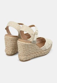 Beige espadrille wedge sandalen met geweven stoffen banden en een gevlochten jute platform, met een gespsluiting en textuurdetails.
