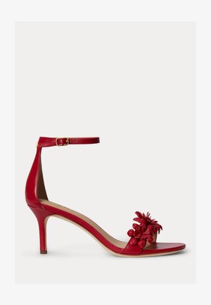 Raudona odinė aukštakulnė basutė su kulkšnies dirželiu ir gėlių dekoracijomis ant priekinės dalies, eksponuojama ant balto fono.