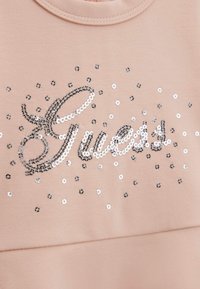 La parola "Sweet" in paillettes su un tessuto rosa chiaro con piccole paillettes argentate e nere sparse attorno al testo.