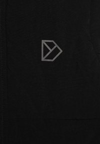 Tissu noir avec une finition texturée présentant un design de logo géométrique gris dans le coin supérieur. Les coutures sont visibles.