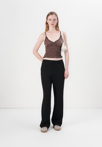 Smeđi, nabrani crop top s čipkastim obrubom u kombinaciji s crnim hlačama visokog struka. Uparen s bež cipelama i malom bijelom torbicom.