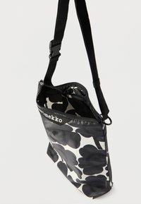 Sort-hvid blomster-mønstret taske med lynlåslukning, justerbar rem og logodetalje. Fremstillet af tekstureret materiale med rummeligt indre.
