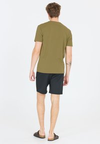 Vihreä oliivinvärinen t-paita, lyhyet hihat, slim fit -malli, yhdistetty mustiin shortseihin, sileä pinta, käytetään tummanruskeiden sandaalien kanssa. Ei huomattavia kuvioita.