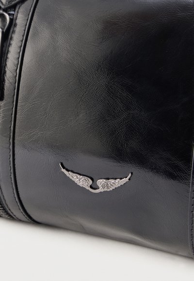 Sac en cuir noir texturé avec emblème d'aile en métal argenté sur le devant, montrant des bords cousus et un détail de fermeture éclair.