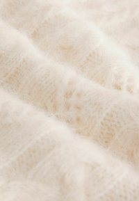 Light cream-colored knitted fabric with a soft, fuzzy texture featuring wavy patterns and a slightly heathered appearance.