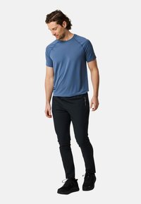 Mannen sportoutfit met een blauw, vochtregulerend shirt met korte mouwen en zwarte tapered broeken, aangevuld met zwarte sportschoenen.
