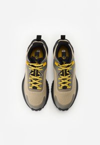 Beżowe i szare sneakersy z teksturowaną cholewką, żółtymi sznurówkami, czarną podeszwą i wzmocnionym noskiem. Zawierają pętlę ułatwiającą zakładanie.