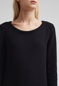 Pull noir texturé avec un col rond et des manches longues, présentant un motif en maille épaisse pour la chaleur et le confort.