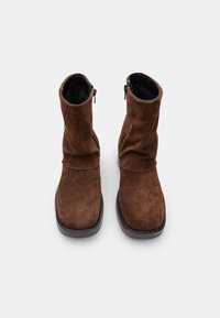 Stivaletti in suede marrone con un design morbido, dotati di una cerniera laterale e di una suola in gomma piatta e testurizzata. Fodera interna liscia.