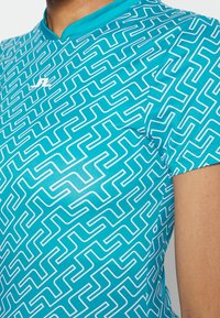 Turkoois sportshirt met een wit zigzagpatroon, korte mouwen en een ronde hals, gemaakt van een soepele, lichte stof.