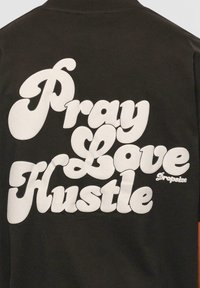 Tricou negru cu un text mare, alb, stilizat, care citește "Pray Love Hustle". Material fin, cu o croială relaxată. Numele brandului "Dropsize" afișat sub text.