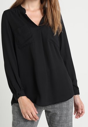 Sort langærmet bluse med v-udskæring, to brystlommer og knapmanchetter. Stoffet har en glat tekstur. Kombinationen er med ternede bukser.
