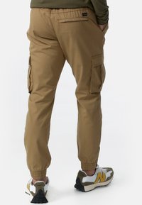 Beige cargobroek met elastische manchetten, zijzakken en een losse pasvorm. Gecombineerd met multicolor sneakers met witte, grijze en gele accenten.