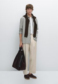 Grijze blouse, witte t-shirt, beige wijde broek, bruine trui om de schouders gedrapeerd, donkerbruine tas en schoenen. Schoon ontwerp.