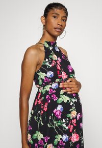 Vestido de maternidade floral com uma base preta, decote halter e flores multicoloridas vibrantes. Tecido suave com um corte confortável.